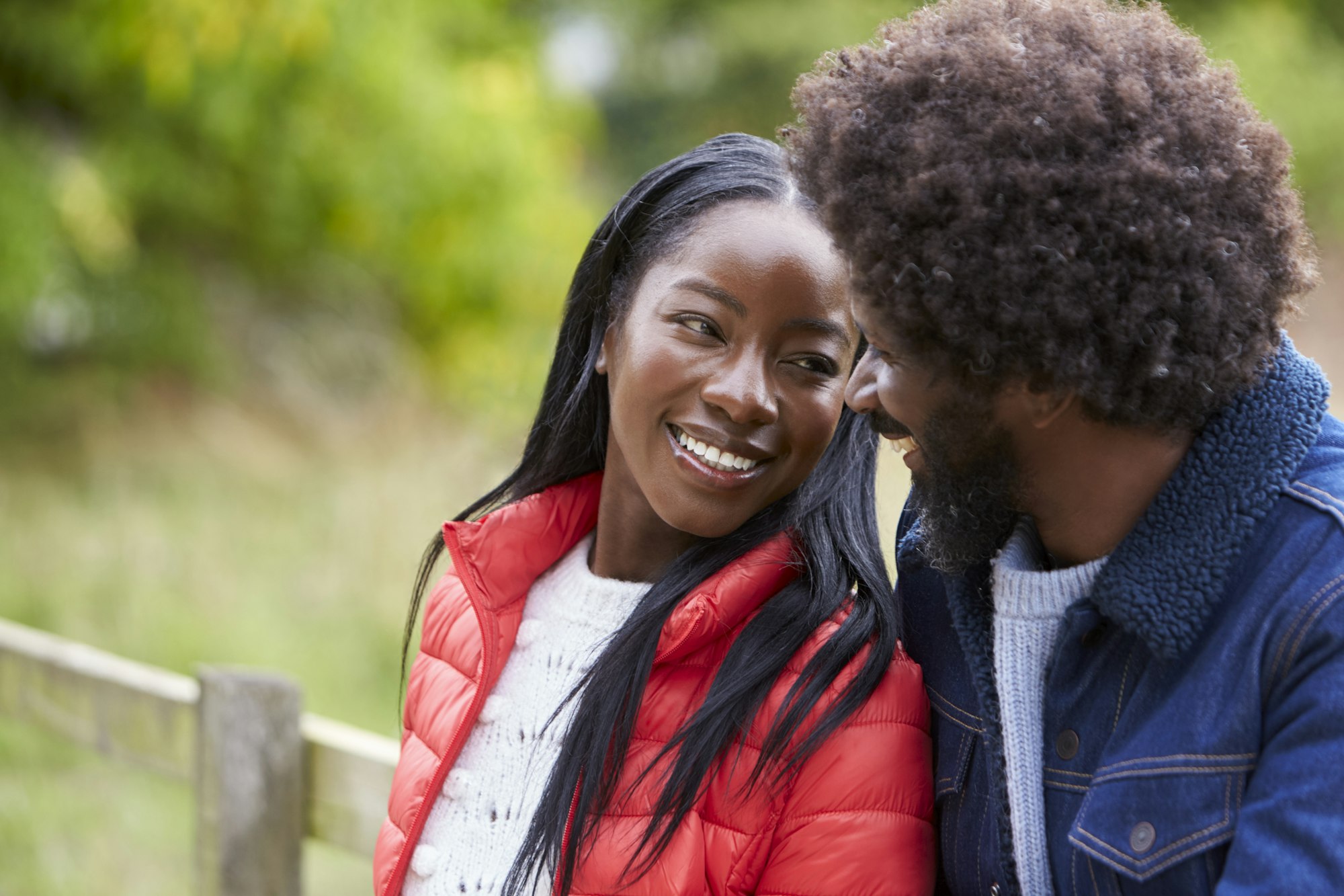 Happy black couple leaning on a fence in the countryside looking into each otherÕs eyes, close up